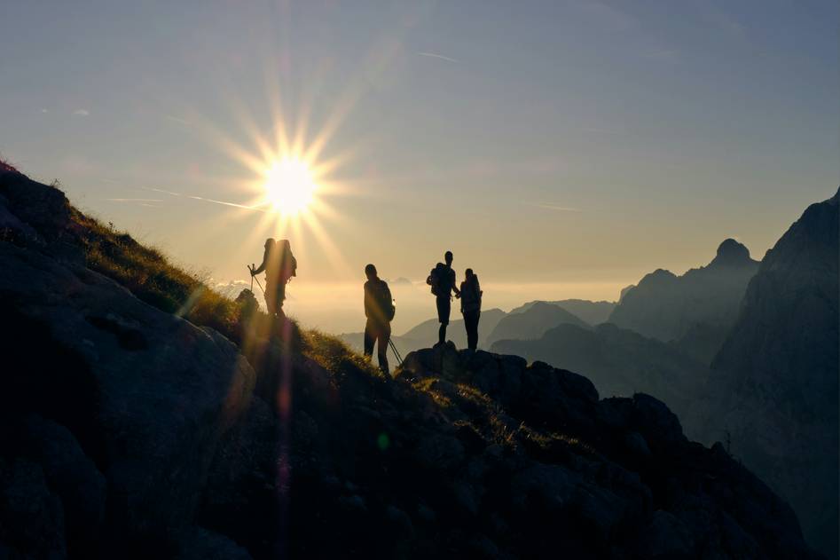Hiker photographing mountain sunrise with mirrorless camera on rocky trail