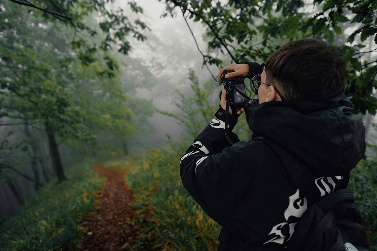 Hiker mounting an action camera for nature hiking on a backpack strap while overlooking mountain valley