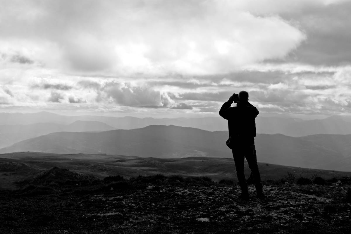 Adventure Photography Ideas featuring a hiker photographing a mountain sunrise with a compact mirrorless camera